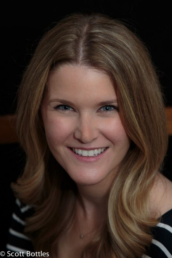 A headshot of a person with long brown hair smiling happily at the camera.